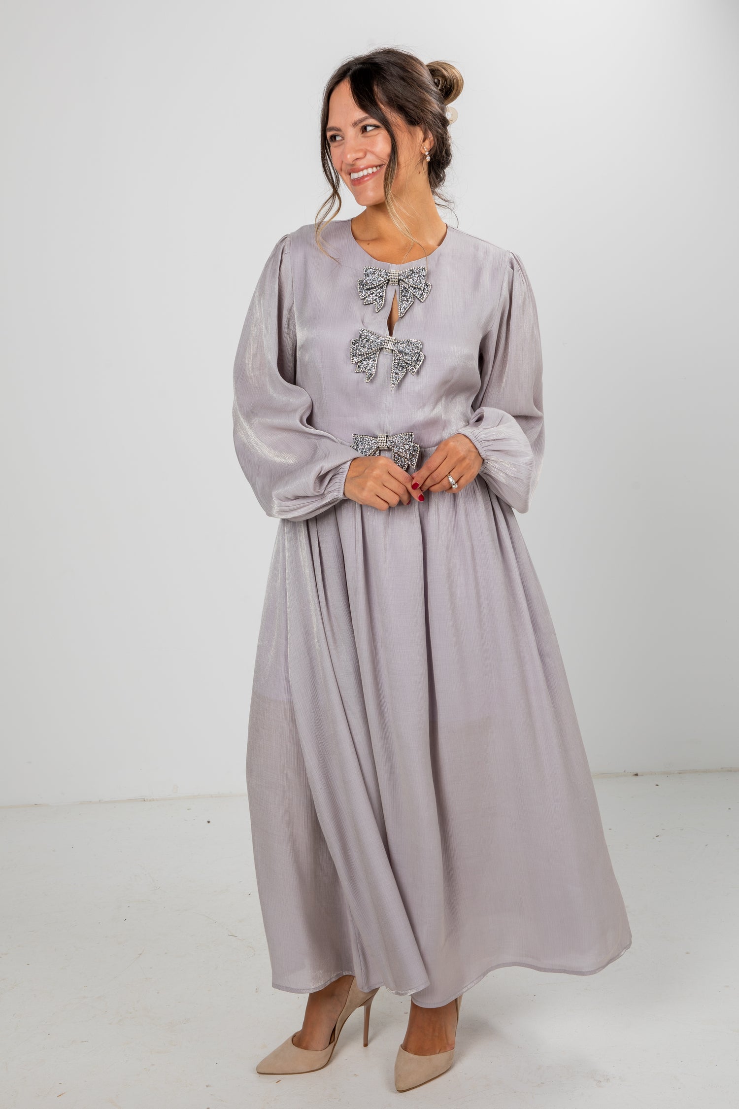 Woman wearing a long light gray dress with decorative elements on a white background