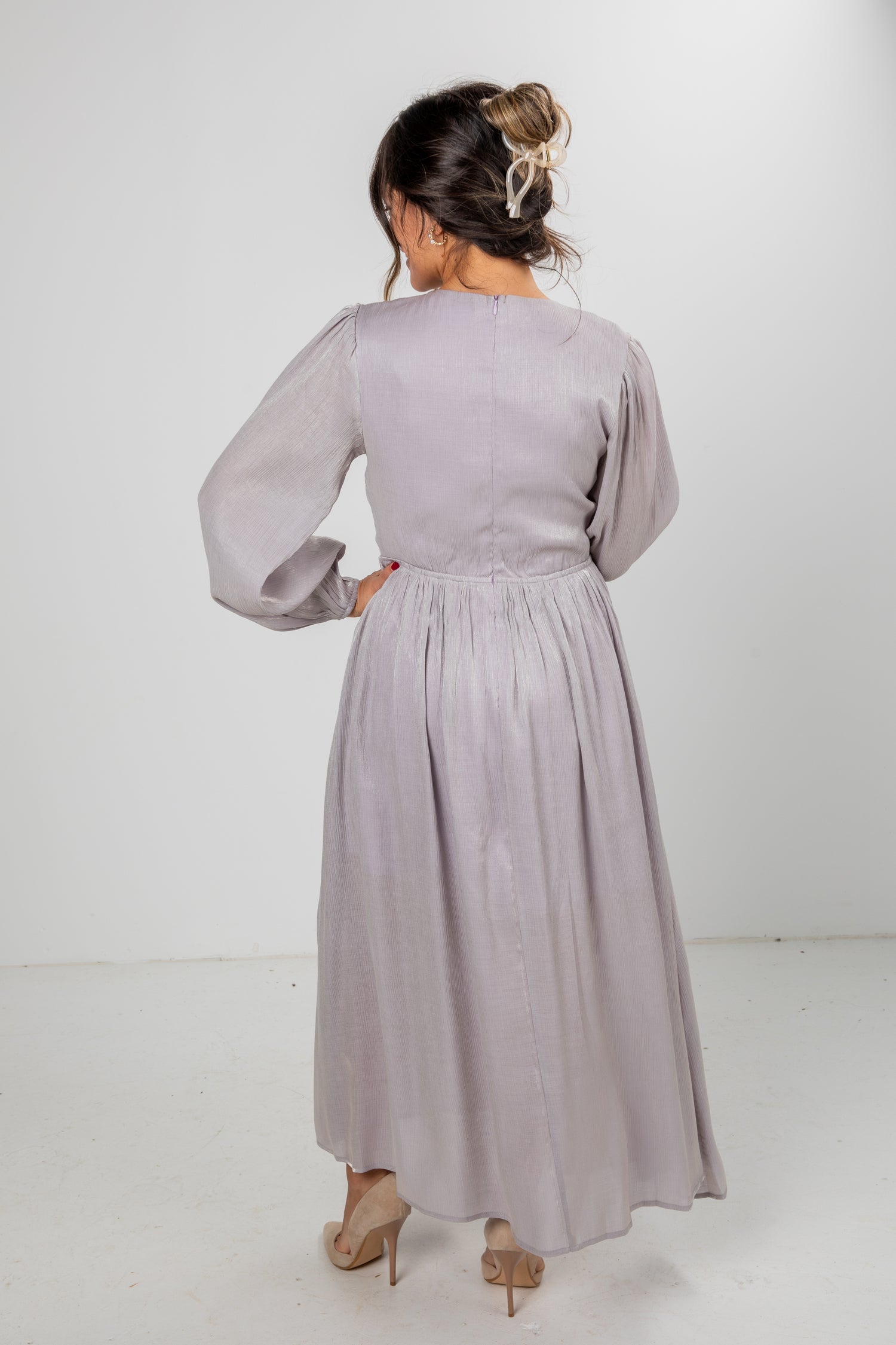 Woman wearing a long light gray dress against a white background