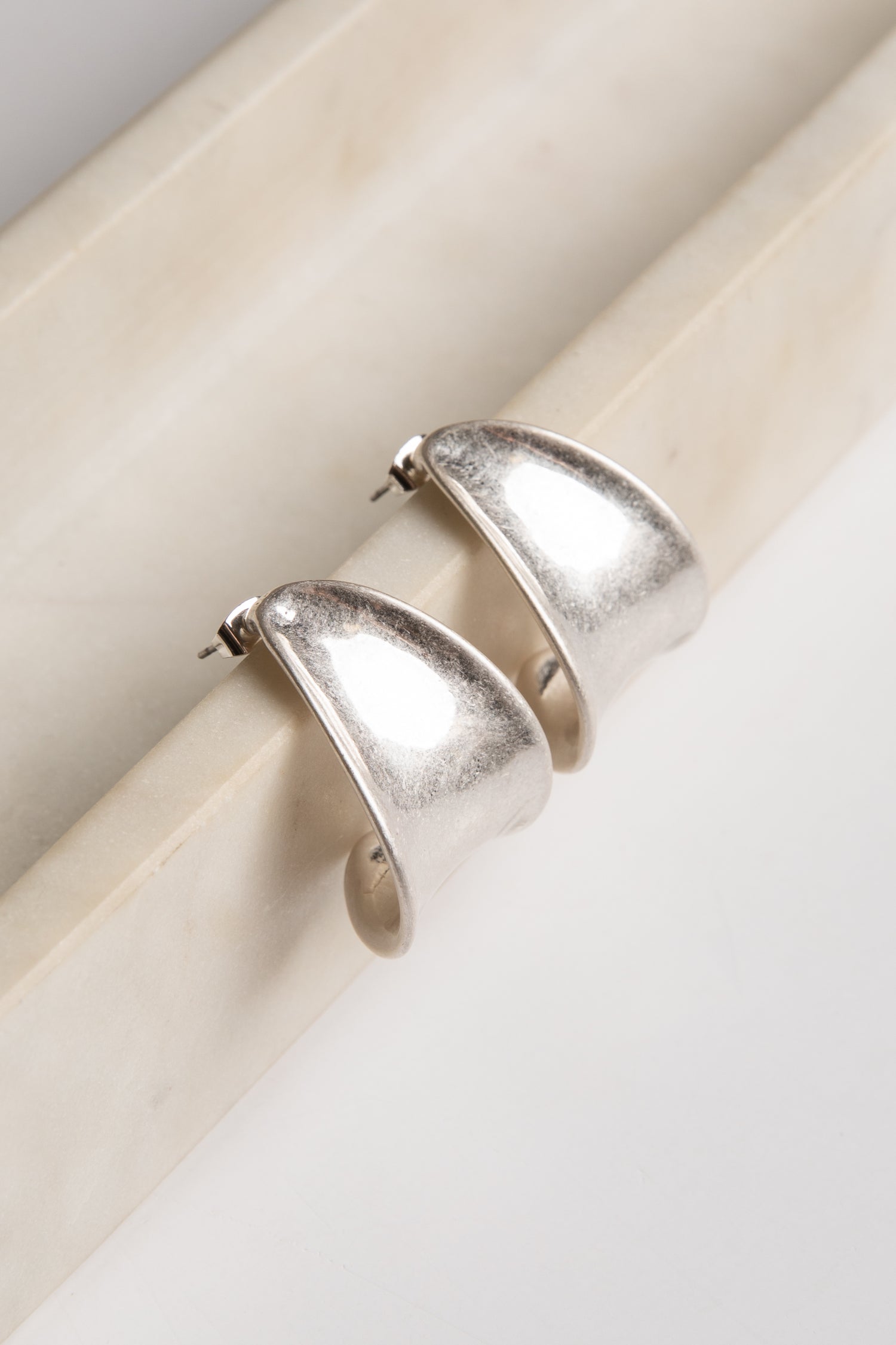 Silver hoop earrings on a beige cylindrical object with a light background