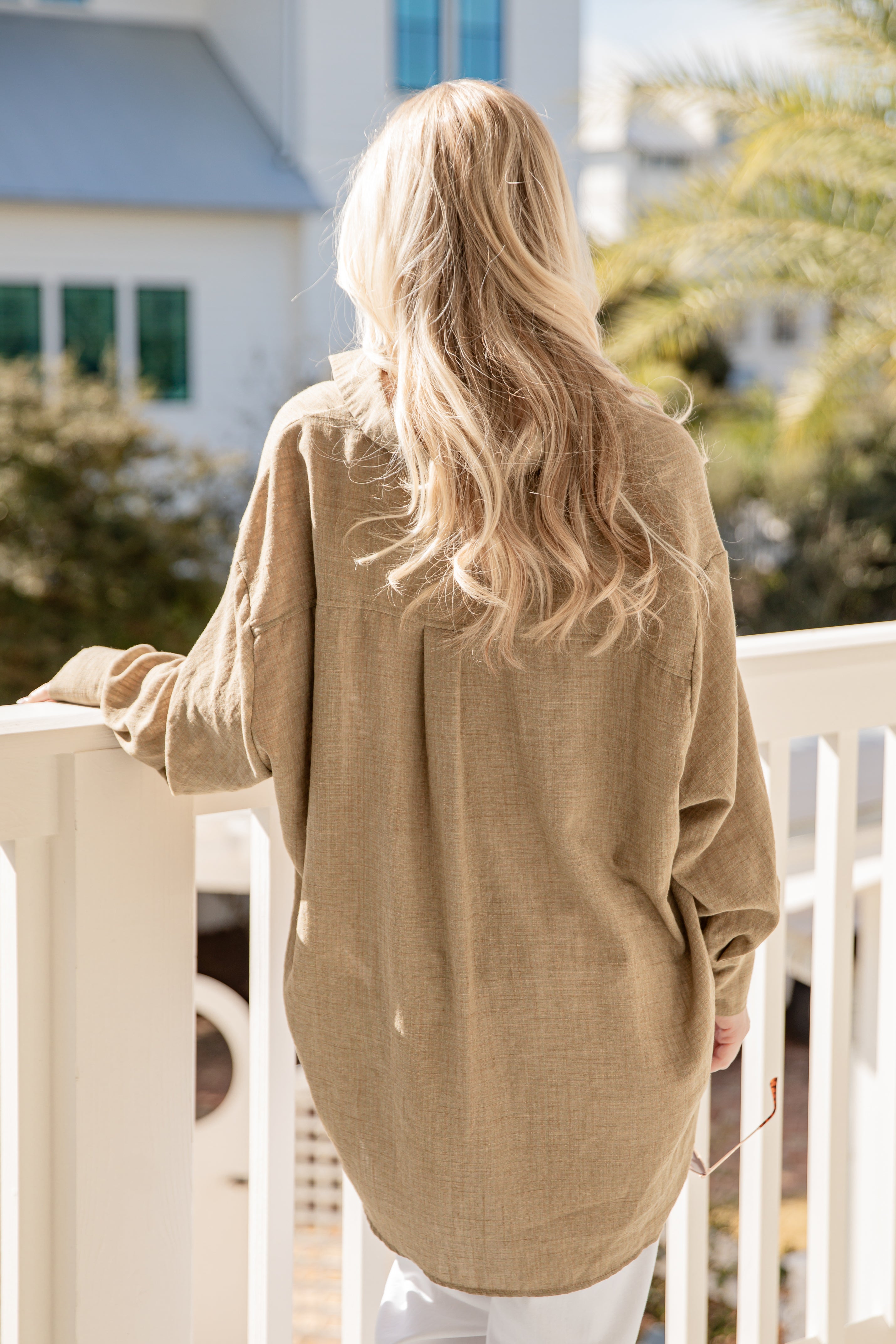 Person wearing a beige sweater standing on a balcony with a blurred background