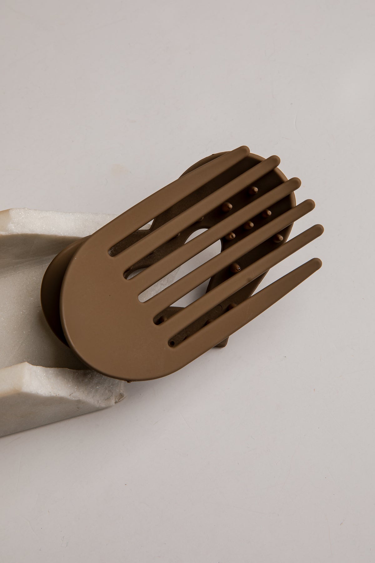 A matte brown hair guard clip with five slotted teeth, shown resting on a white textured foam block against a light gray background.