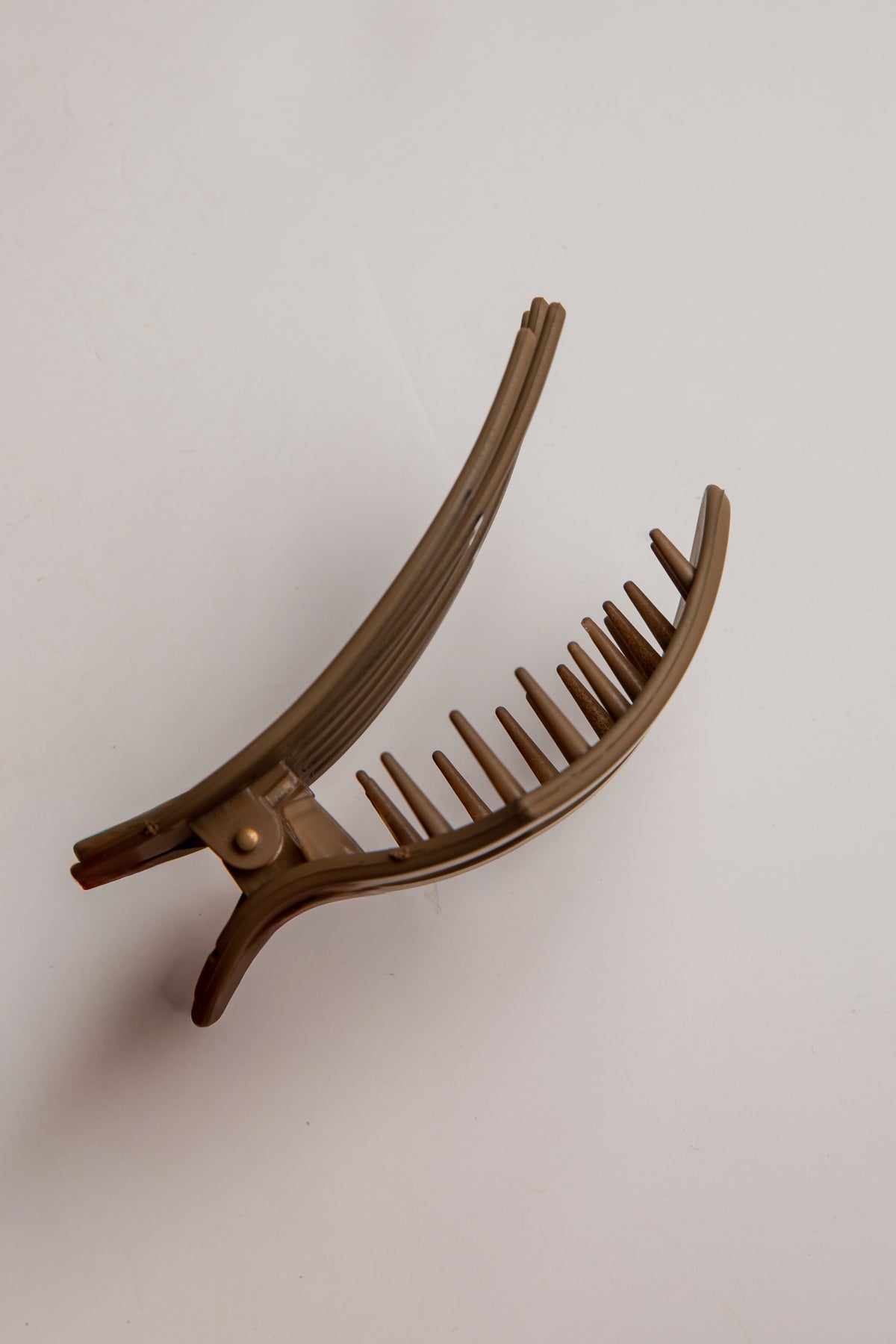 A curved hair claw clip with a glossy brown finish, photographed on a plain off-white background.