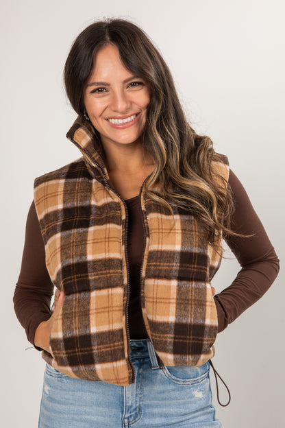 Woman wearing a plaid vest over a brown long-sleeve shirt with a white background