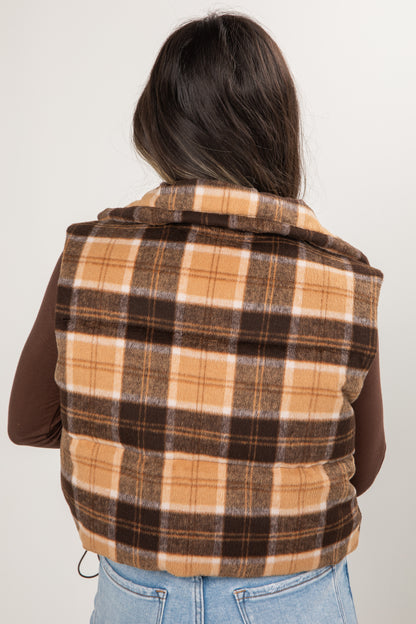 Person wearing a plaid vest over a brown shirt and blue jeans on a white background