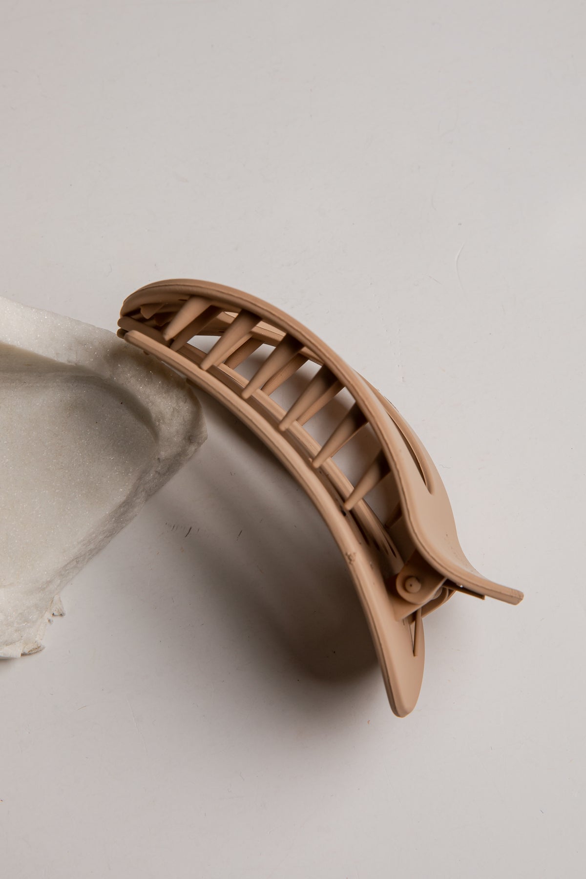 A light beige plastic claw hair clip, shown open on a neutral light gray background.