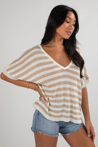 Woman wearing a beige and white striped top with denim shorts on a plain background