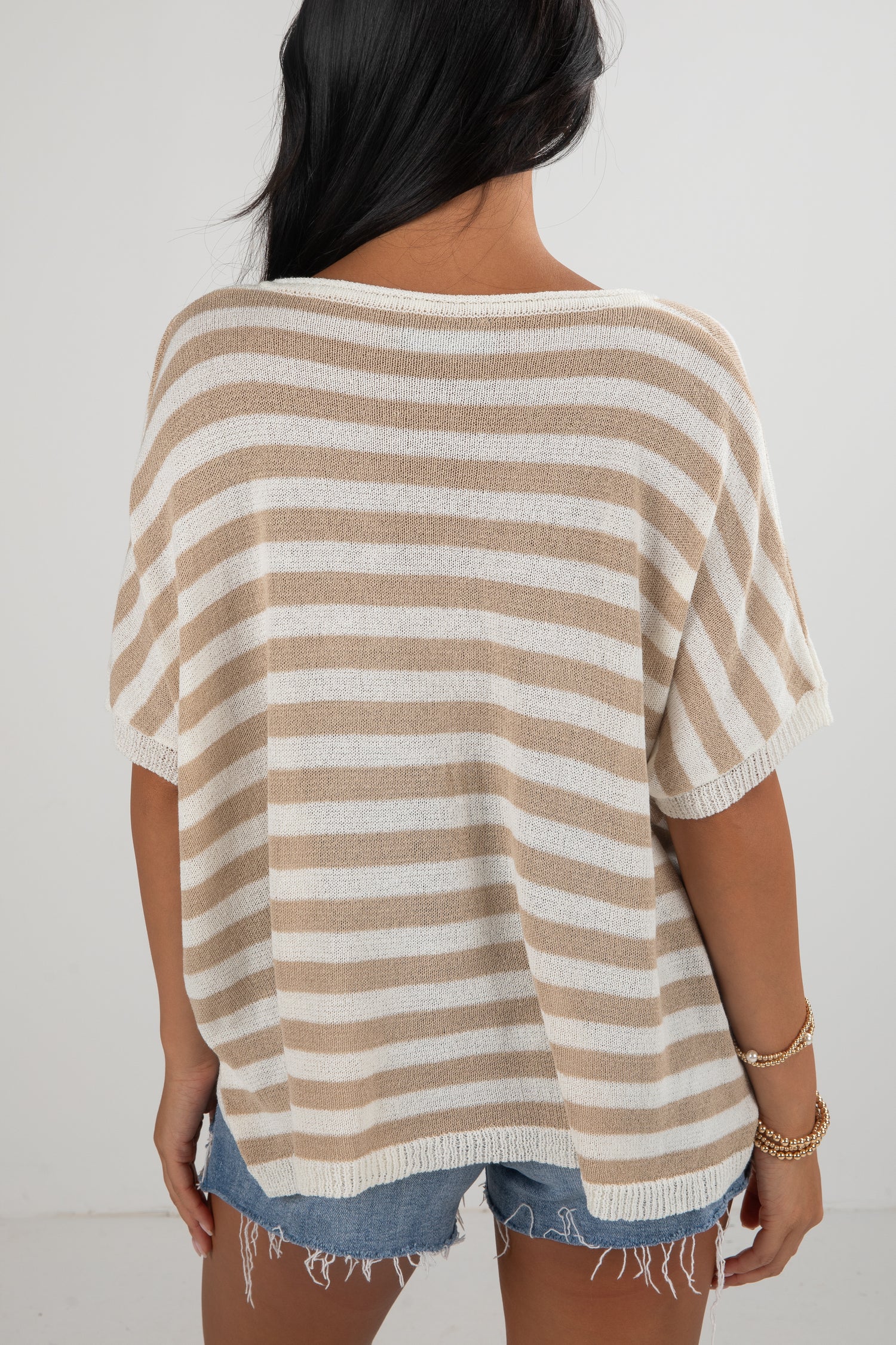 Woman wearing a beige and white striped sweater with denim shorts on a plain background