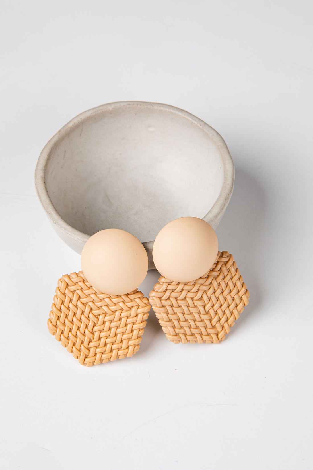 Pair of earrings with woven design and round beige stones on a light gray background