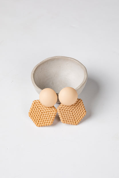 Pair of earrings with woven design and wooden beads on a light gray background