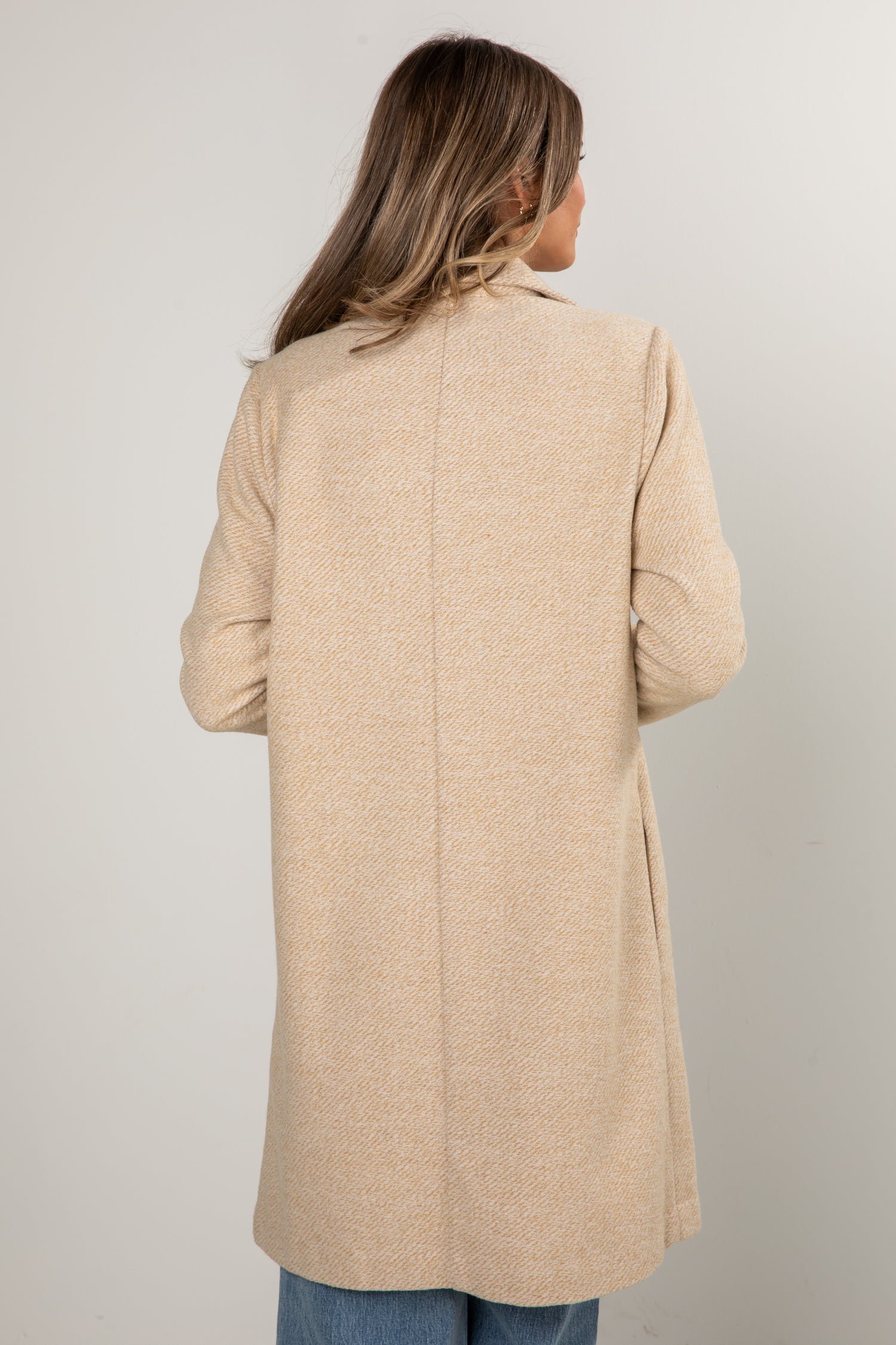 Person wearing a beige coat against a plain background