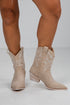 Beige cowboy boots worn by a person on a white background