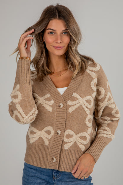 Woman wearing a beige cardigan with bow patterns on a plain background
