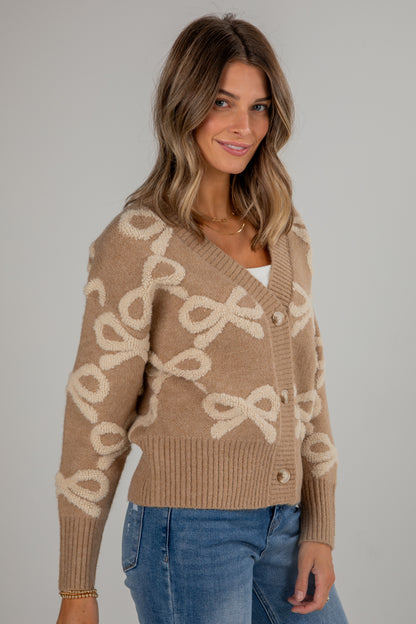 Woman wearing a beige sweater with bow pattern against a gray background