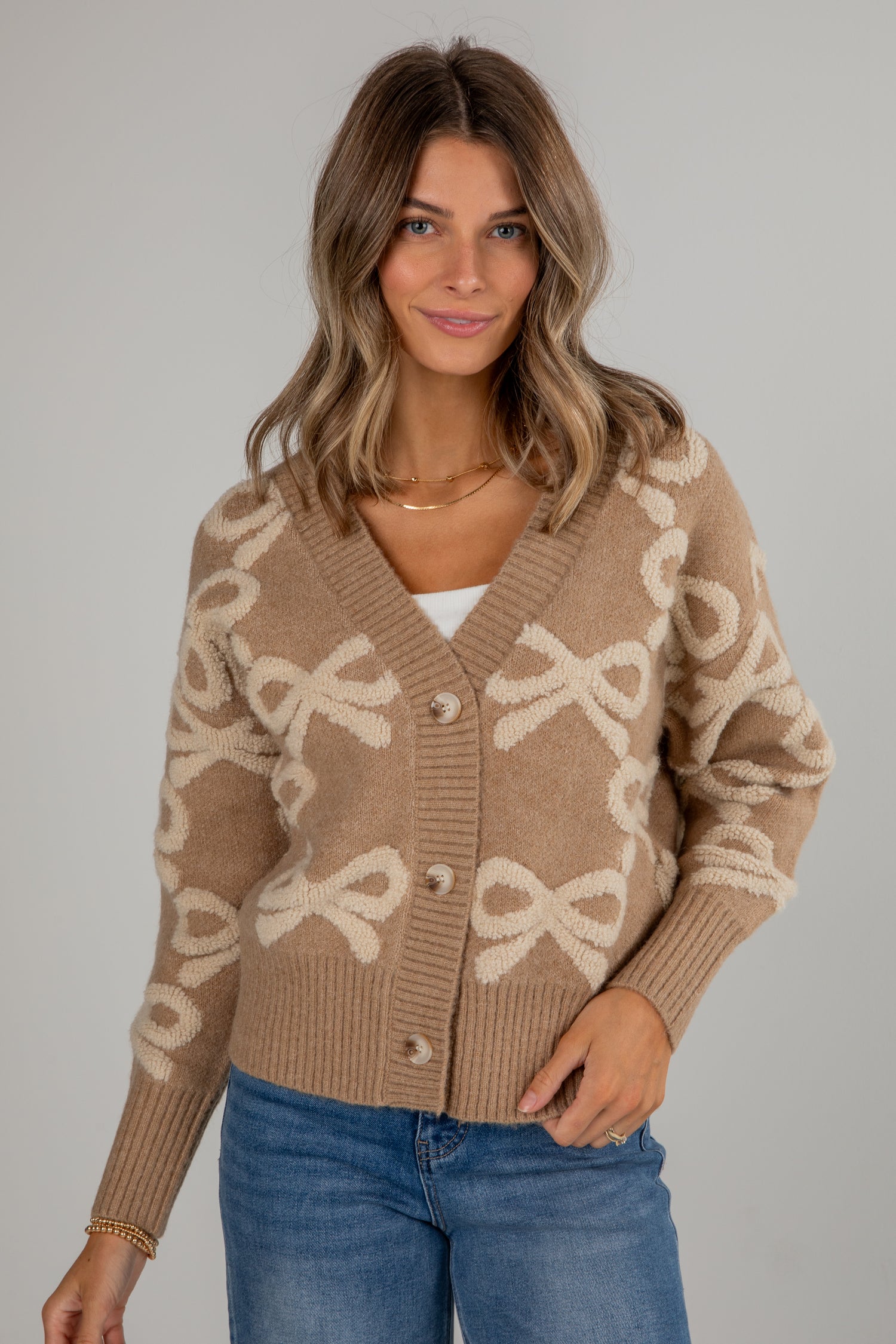 Woman wearing a beige cardigan with bow pattern against a gray background