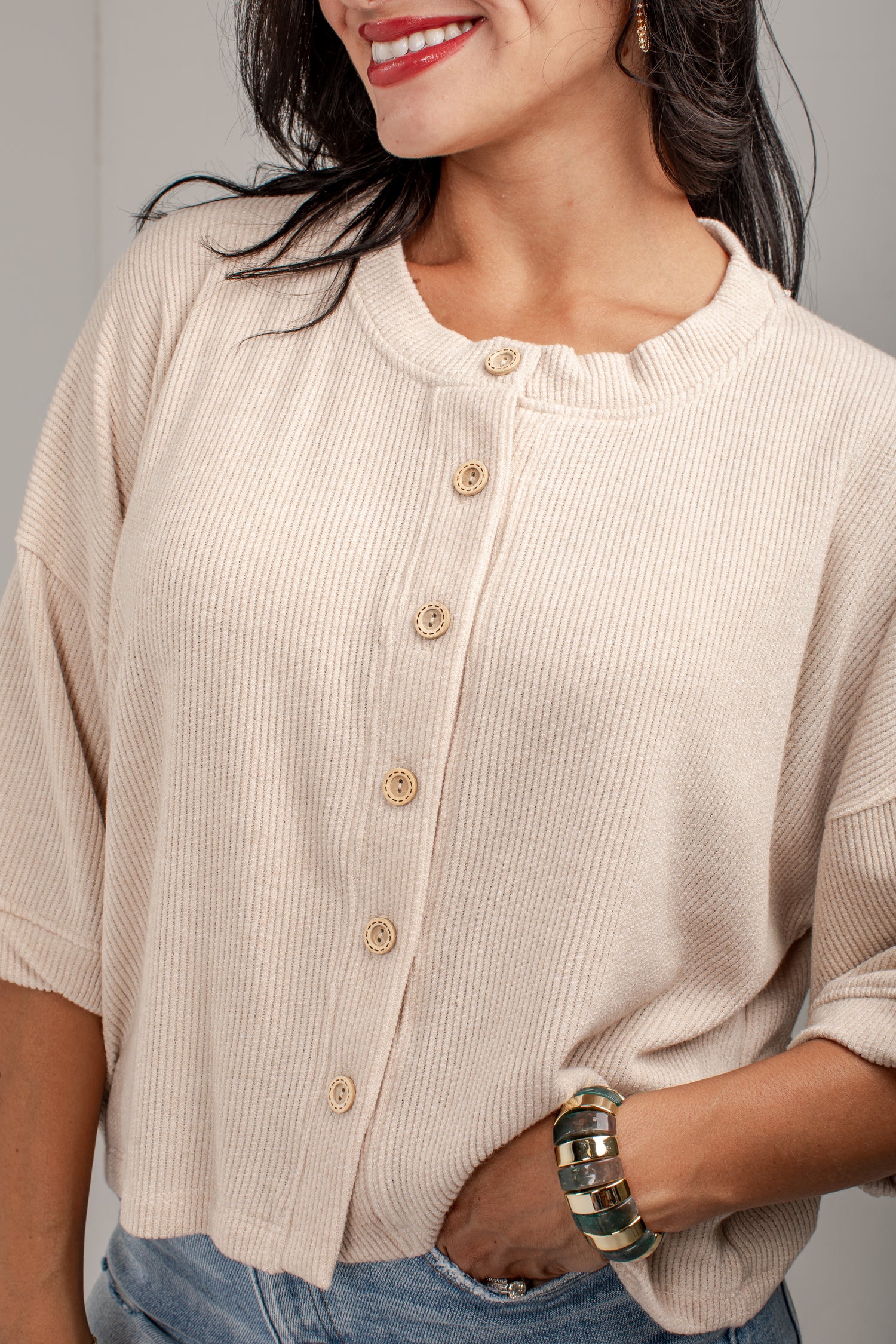 A close-up of a woman wearing a cream-colored ribbed knit cardigan with a button-down front and light wood buttons, paired with blue jeans.