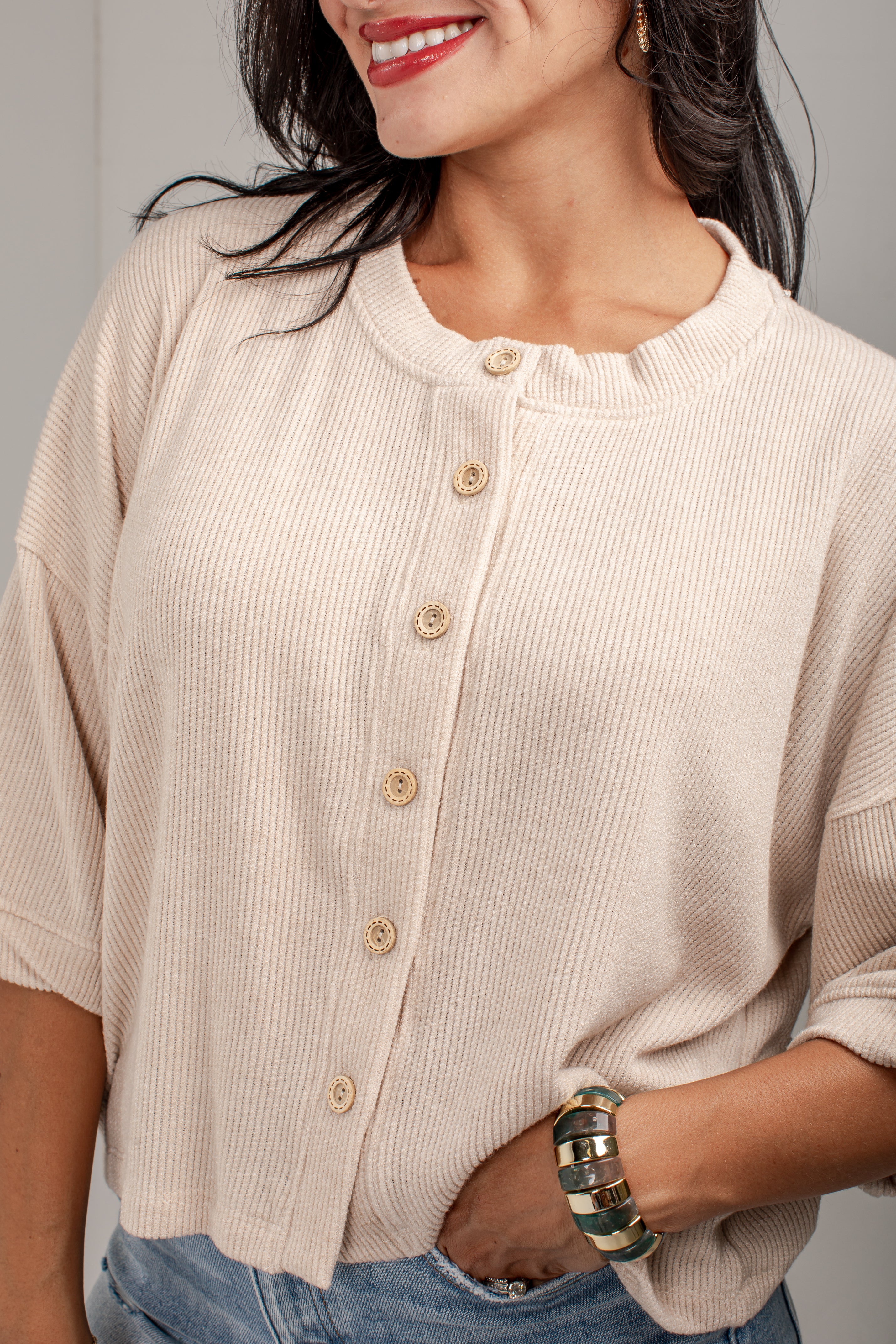 A close-up of a woman wearing a cream-colored ribbed knit cardigan with a button-down front and light wood buttons, paired with blue jeans.