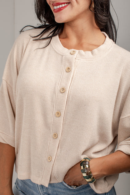 A close-up of a woman wearing a cream-colored ribbed knit cardigan with a button-down front and light wood buttons, paired with blue jeans.