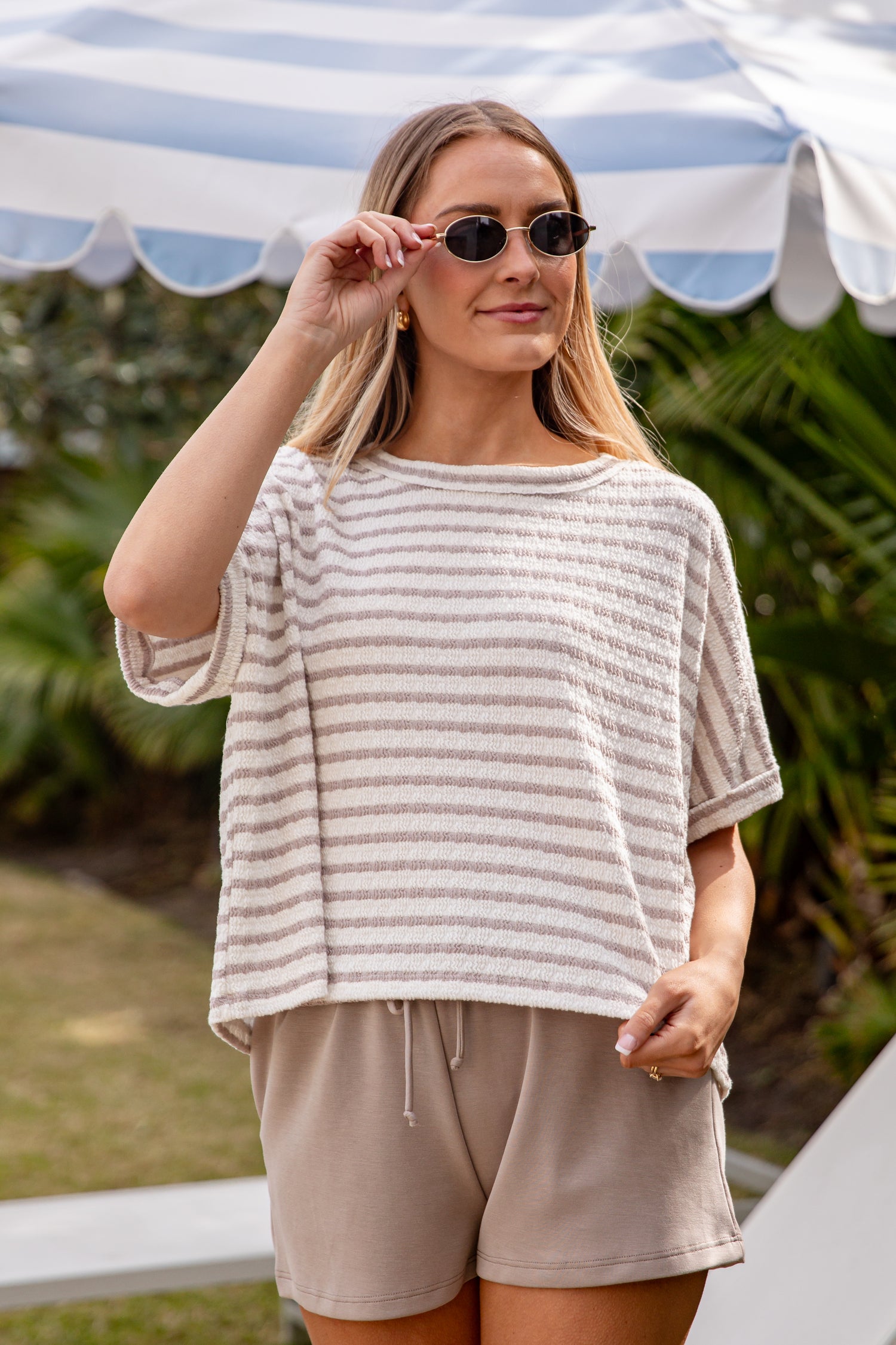 Woman wearing a striped shirt and shorts outdoors with a striped canopy in the background