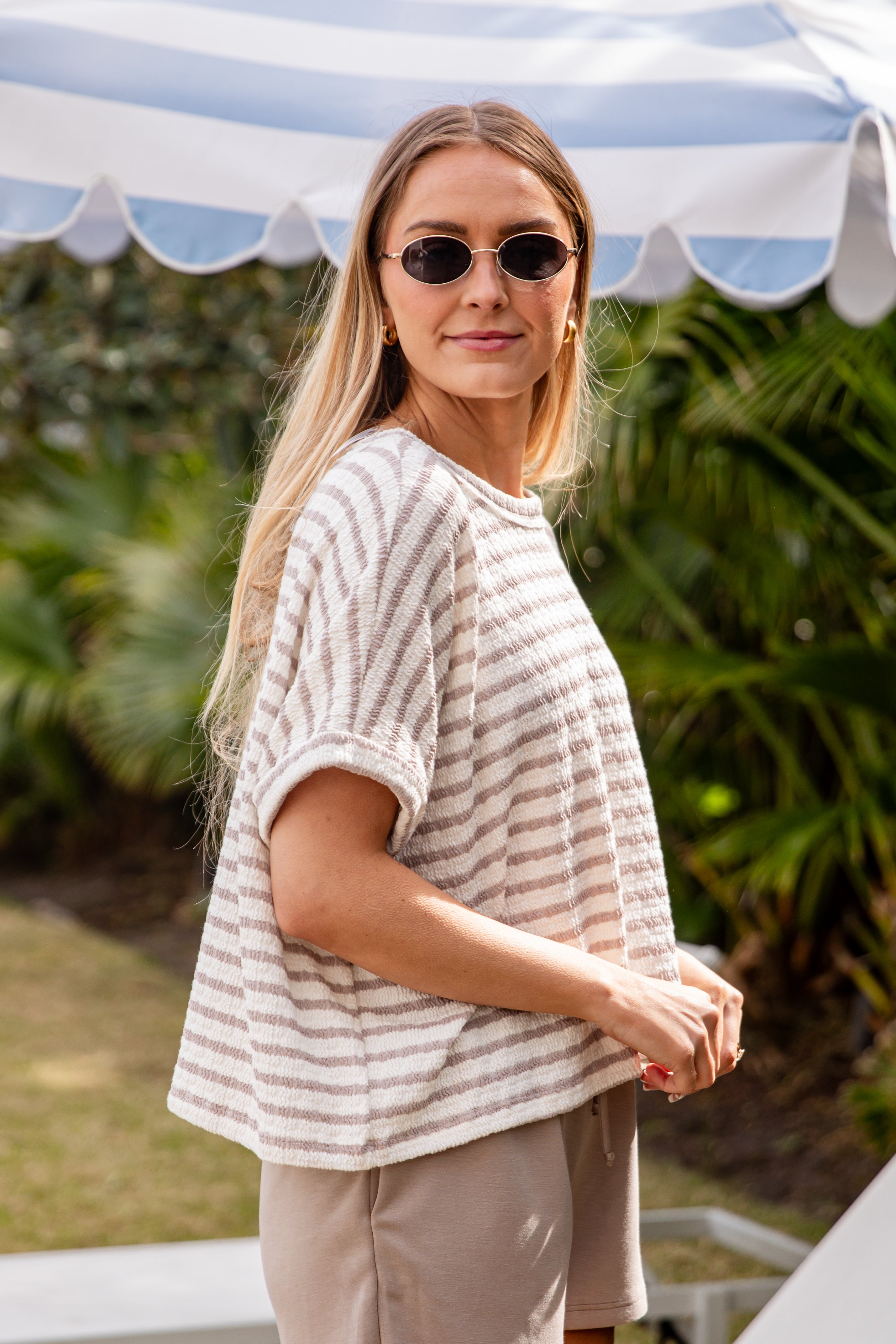 Woman wearing a striped shirt and sunglasses outdoors with greenery in the background