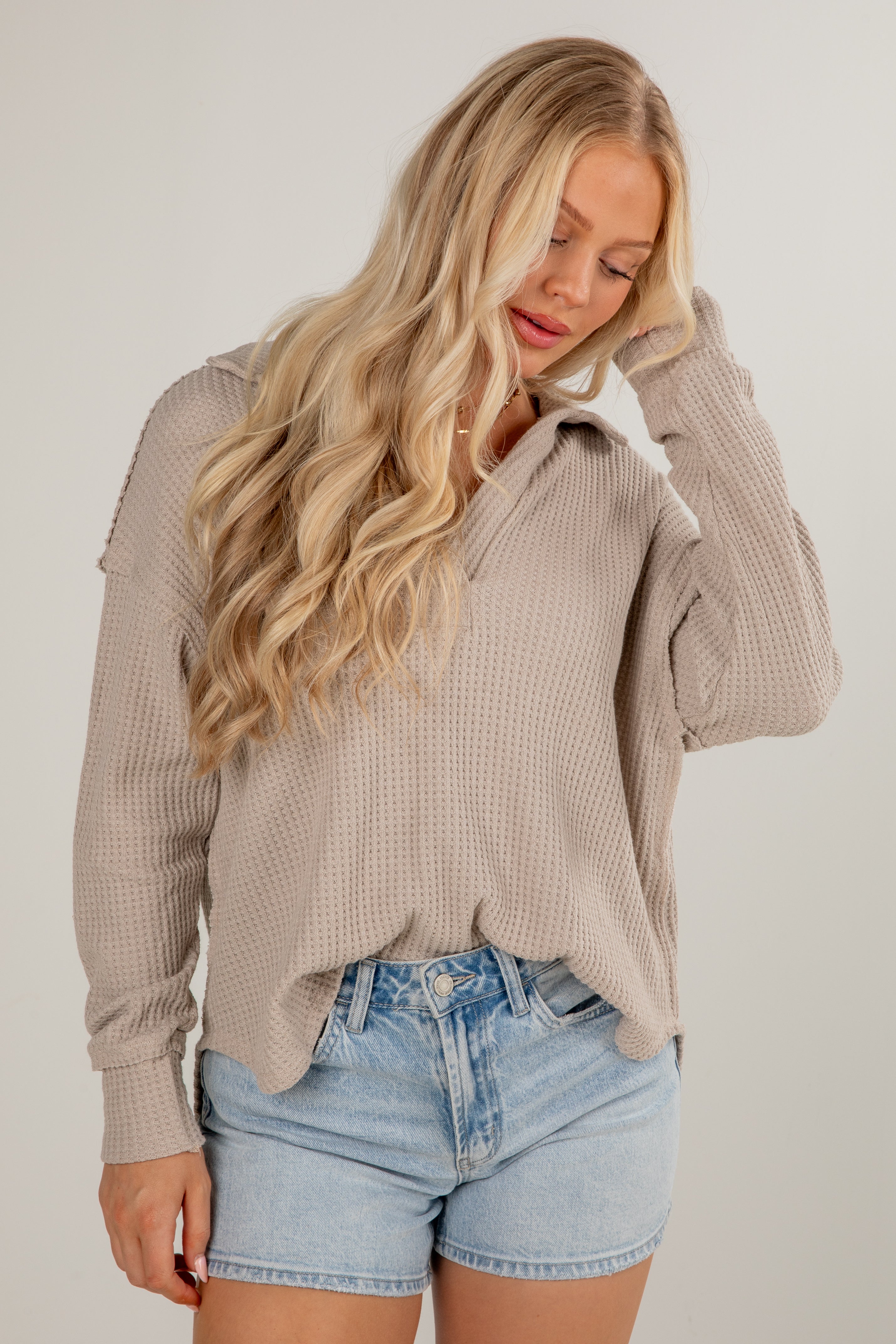 Woman wearing a beige ribbed sweater and denim shorts on a plain background
