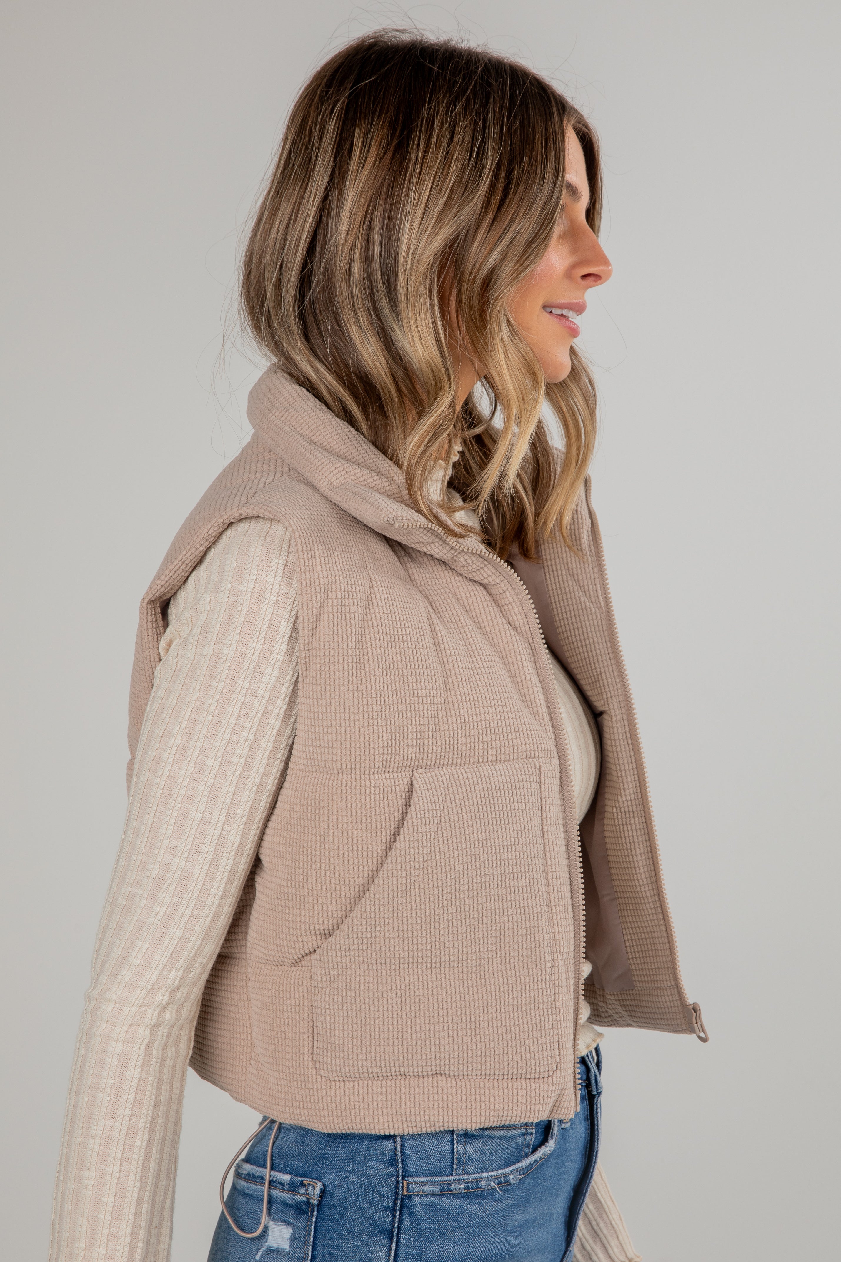Woman wearing a beige vest over a sweater with a plain background