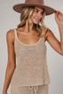 A woman wearing a beige open-knit sleeveless tank top and matching bottoms, paired with a brown wide-brim hat, photographed against a light gray studio background.