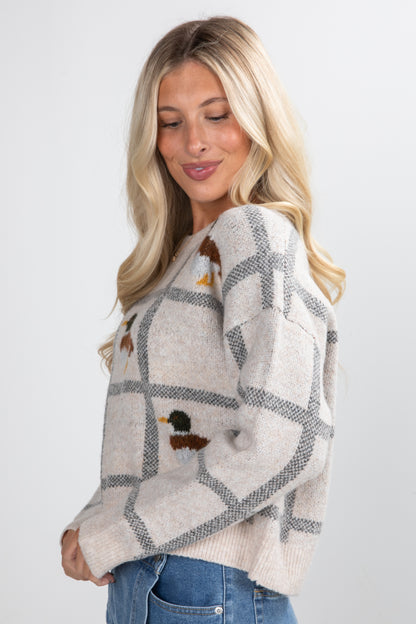 Woman wearing a patterned sweater with duck designs on a plain background