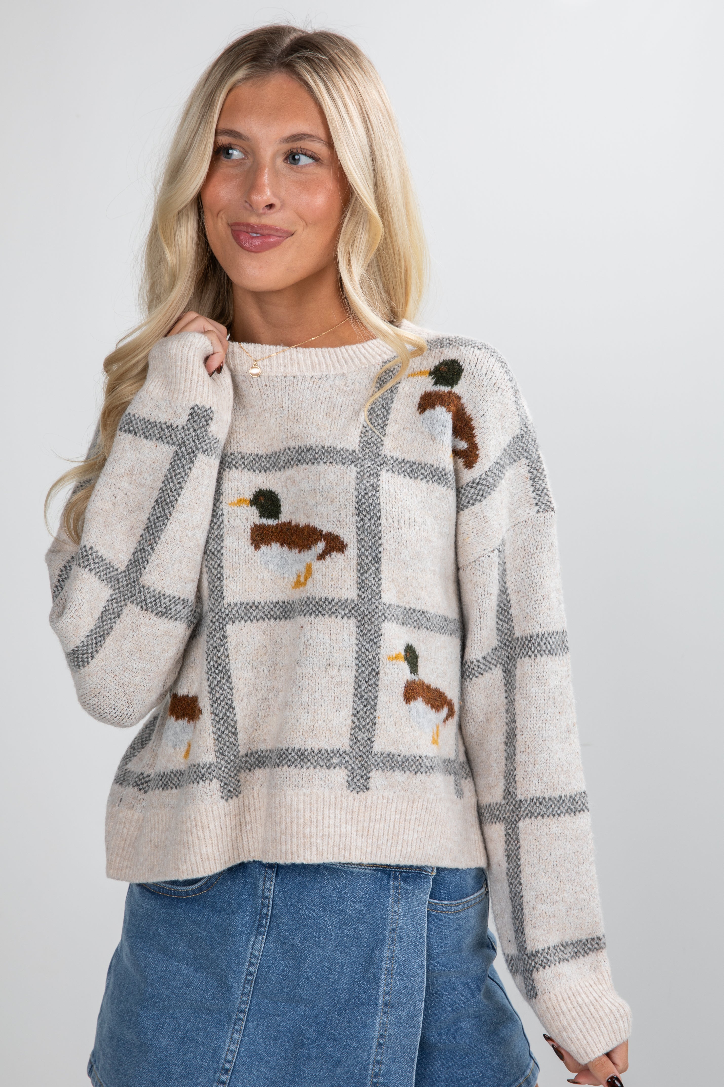 Woman wearing a plaid sweater with duck designs on a plain background