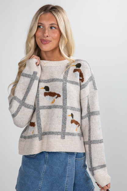 Woman wearing a plaid sweater with duck designs on a plain background