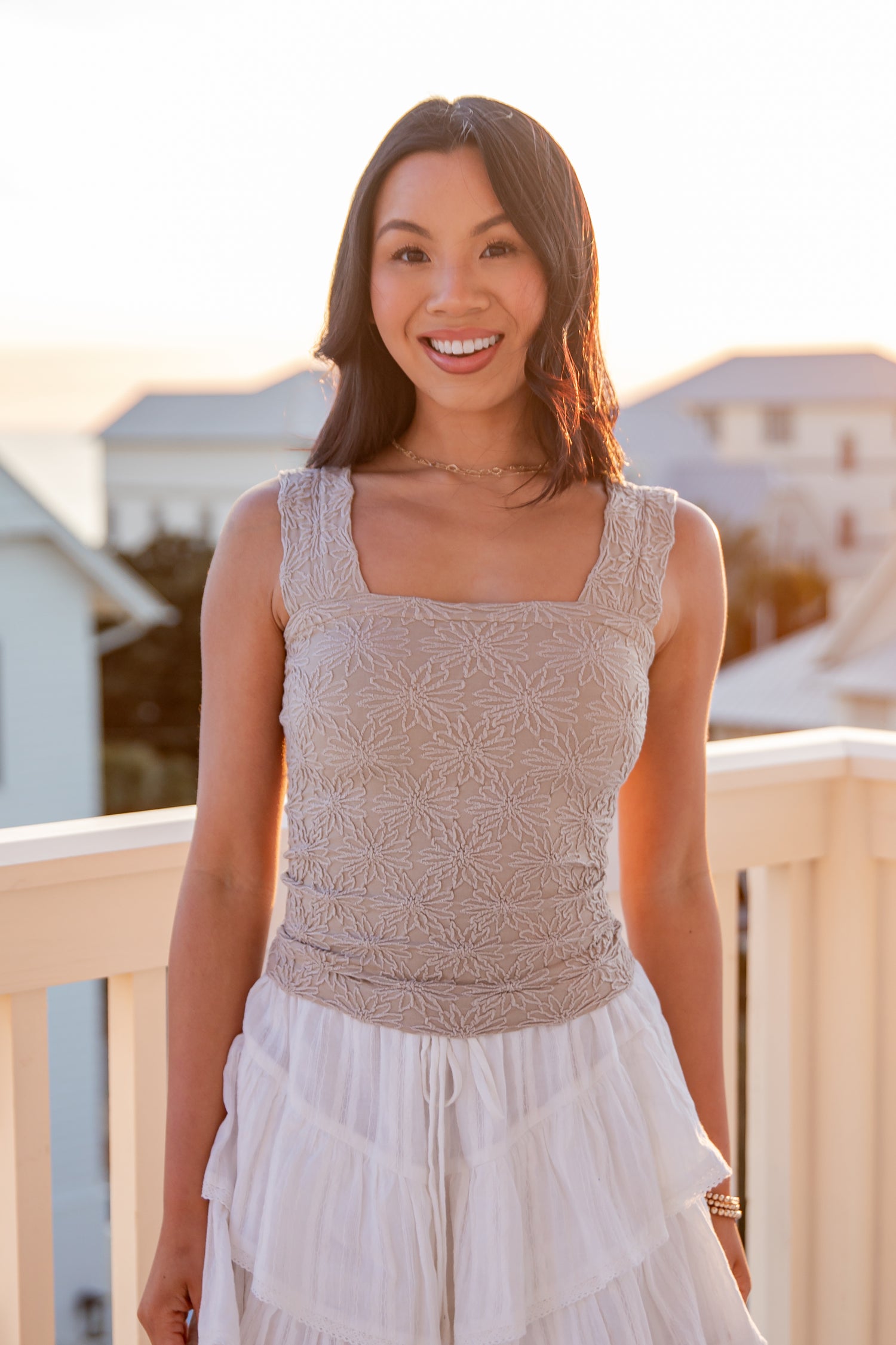 Woman wearing a sleeveless patterned top and white skirt on a balcony with a blurred background