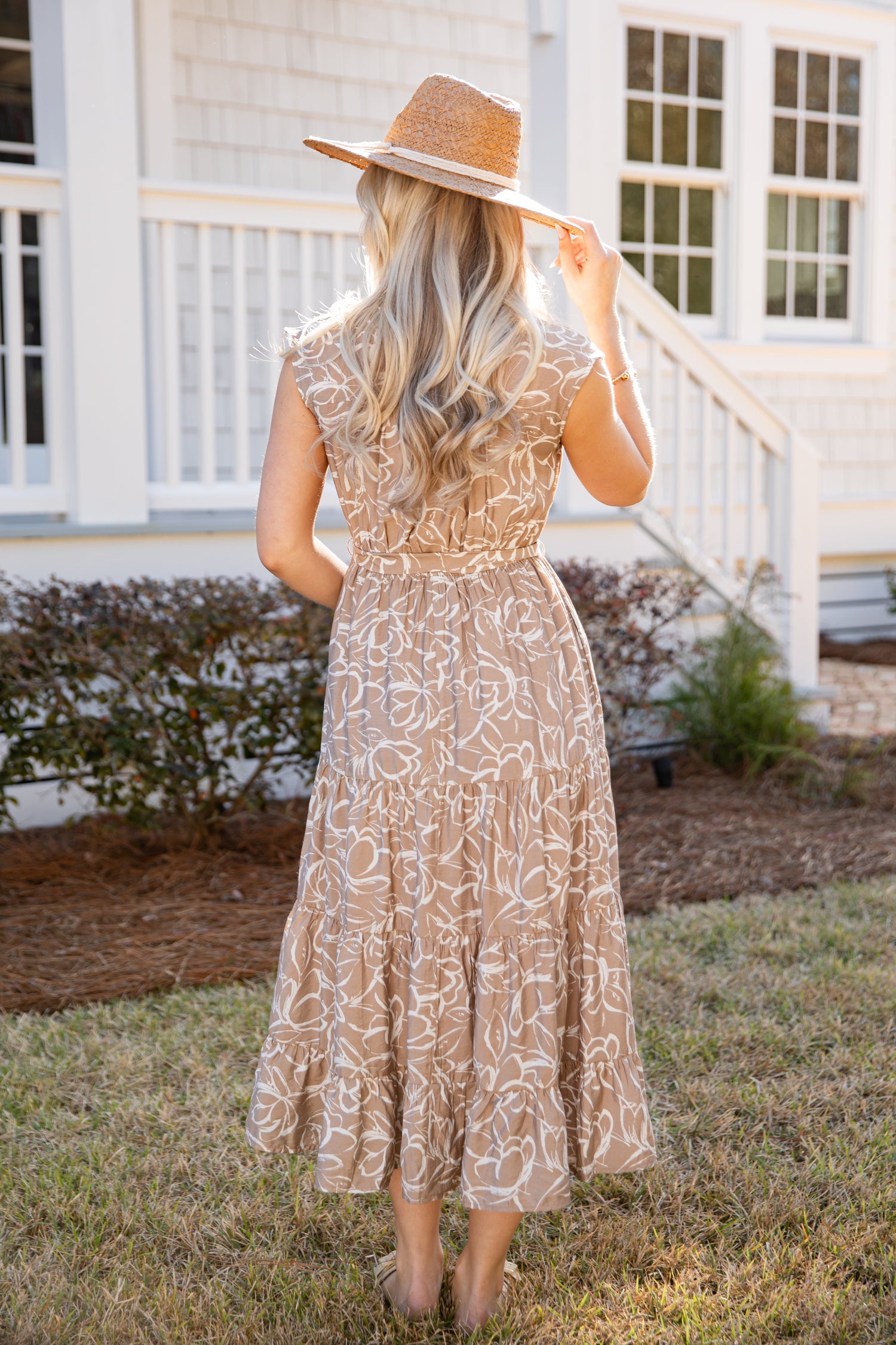 Woman in a lace dress and straw hat standing in front of a white house.