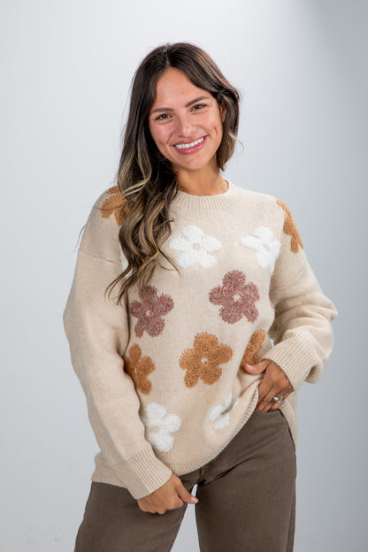 Woman wearing a beige sweater with floral patterns on a plain background
