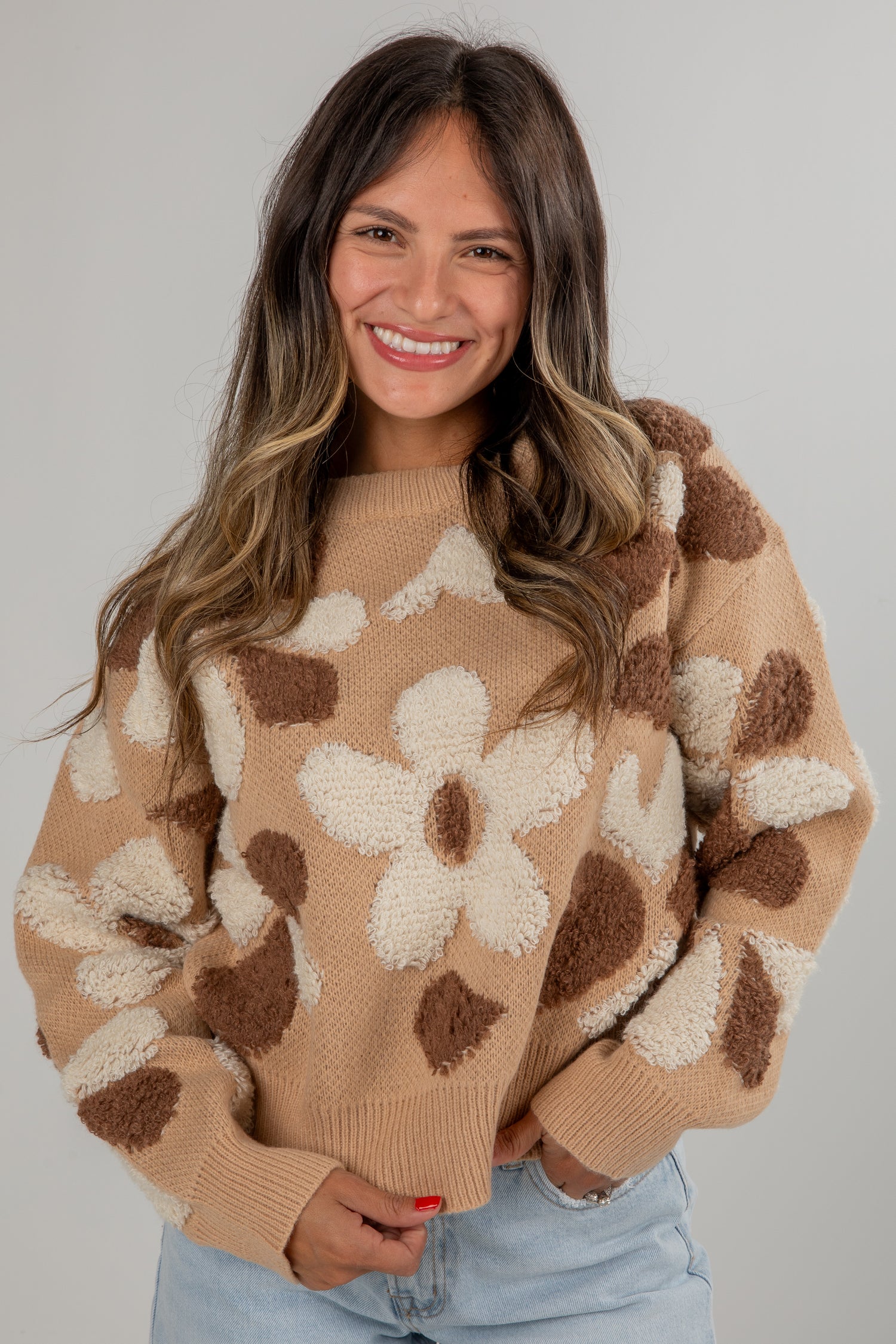 Woman wearing a beige sweater with floral patterns against a plain background