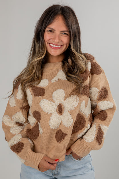 Woman wearing a beige sweater with floral patterns against a plain background