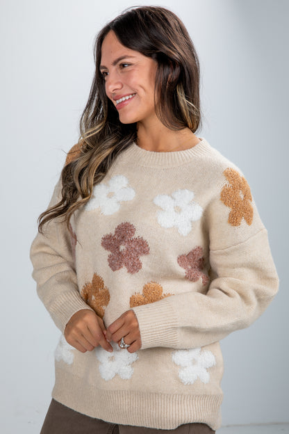 Woman wearing a beige sweater with floral patterns on a plain background