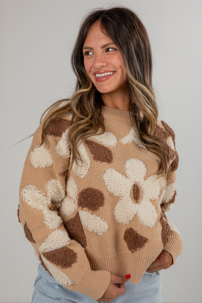 Woman wearing a beige sweater with brown and white floral patterns against a plain background