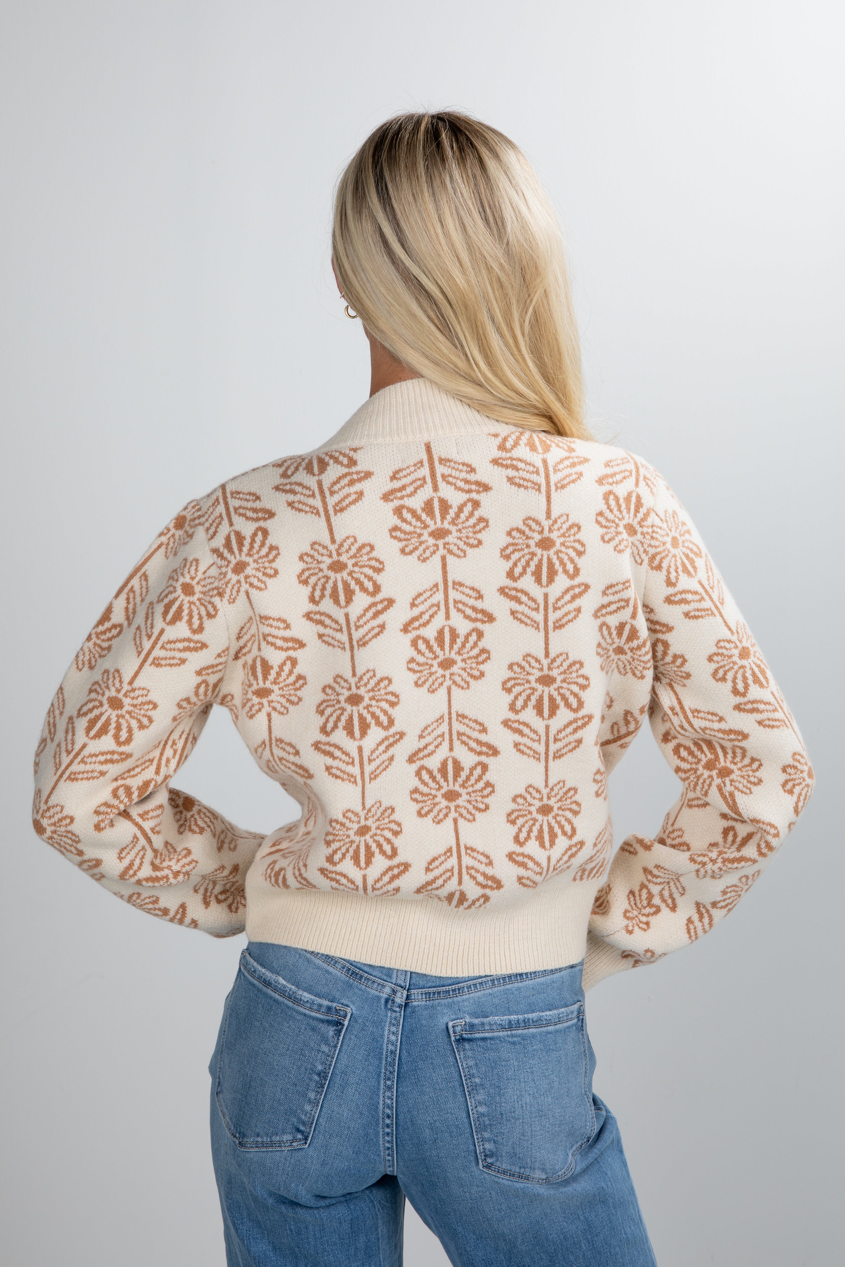 Person wearing a floral-patterned cardigan and blue jeans on a plain background