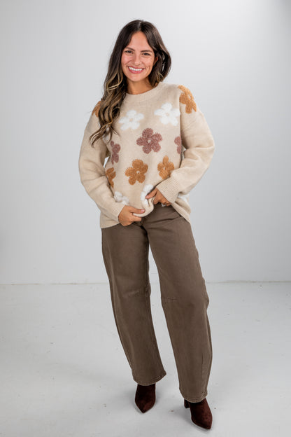 Woman wearing a beige sweater with floral patterns and brown pants on a white background