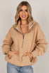 A woman modeling a beige half-zip hoodie with a drawstring hood and front pockets, paired with light blue jeans, against a plain light gray studio background.