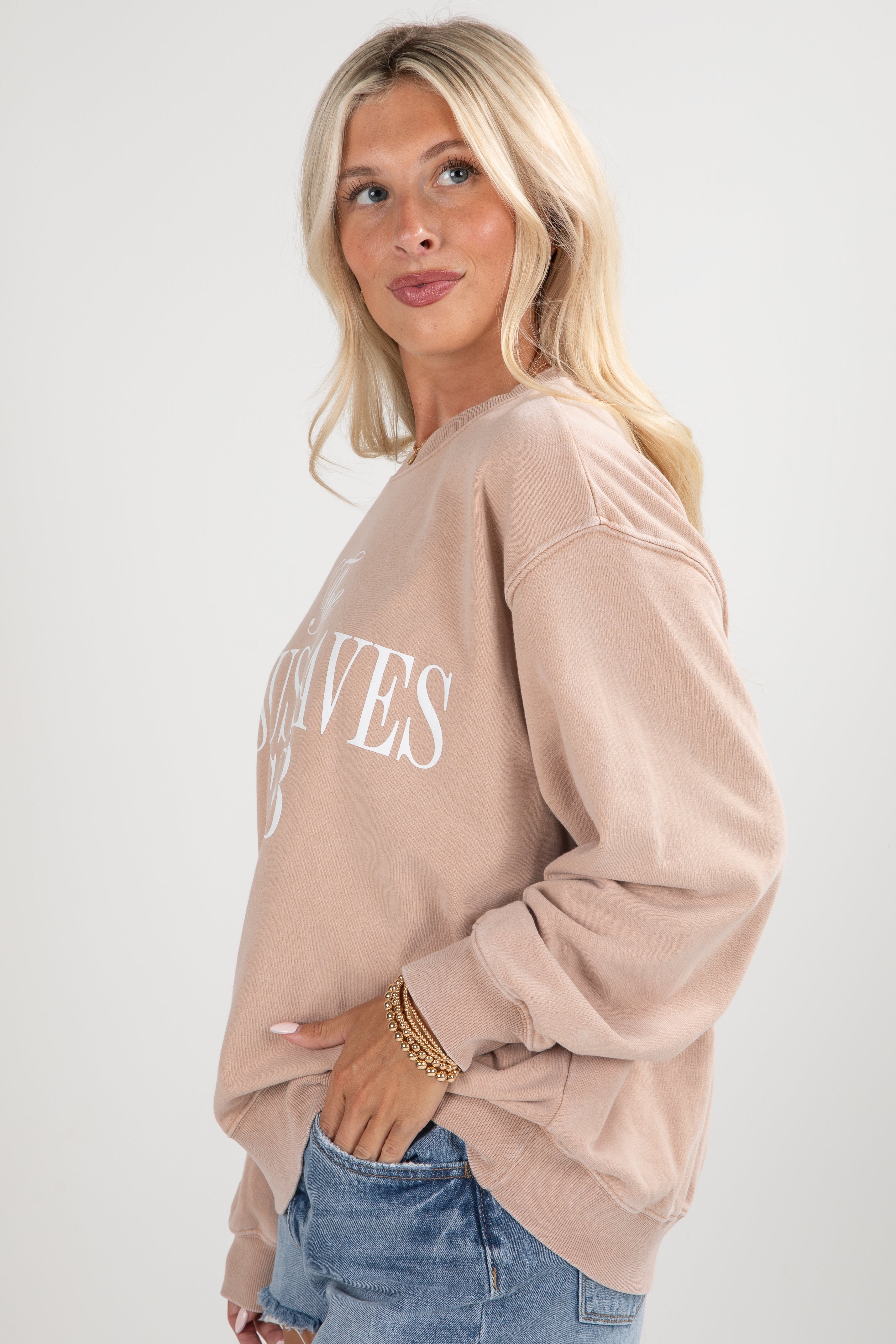 Woman wearing a beige sweatshirt with text on a plain background