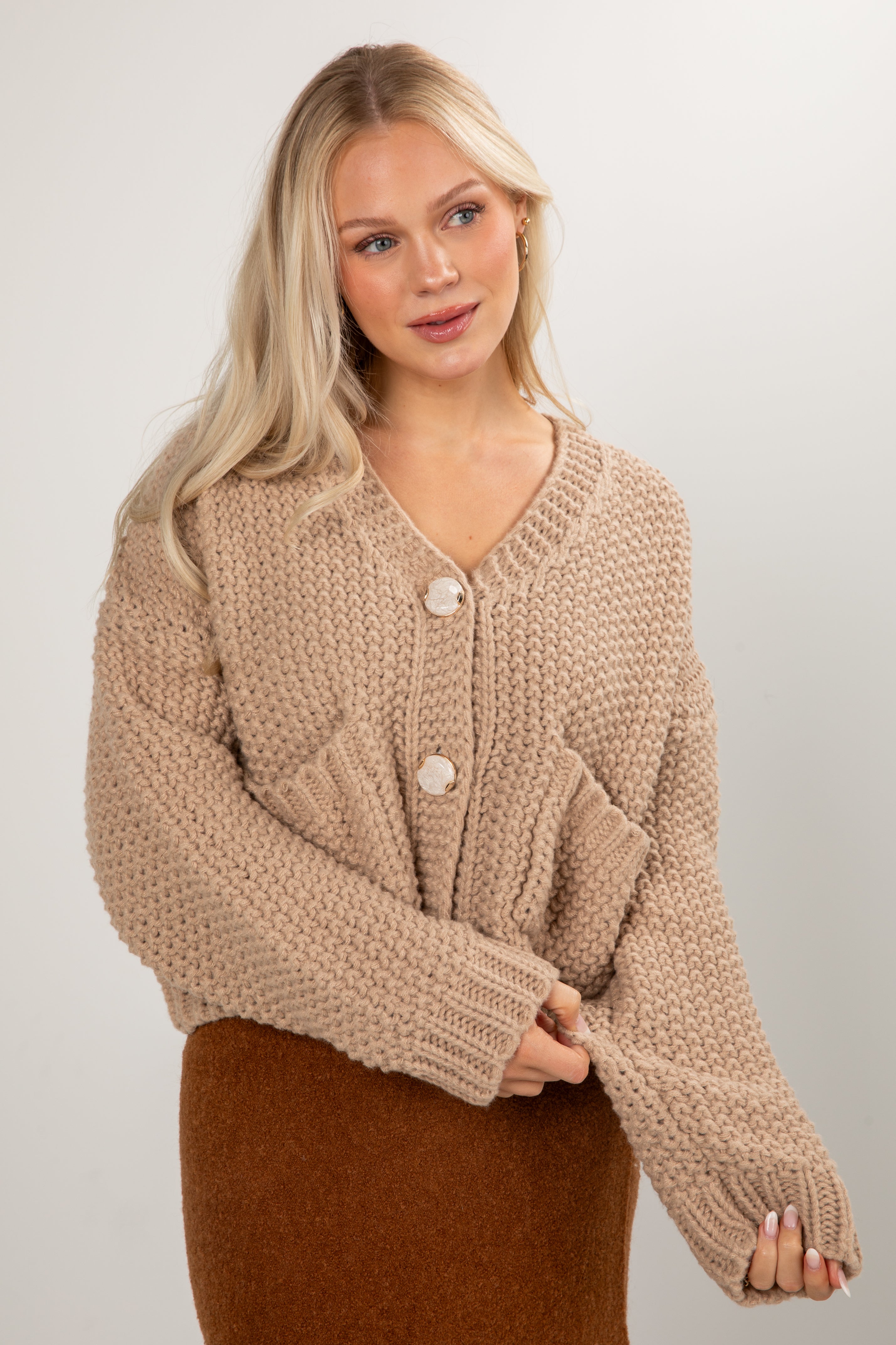 Woman wearing a beige knitted cardigan against a plain background