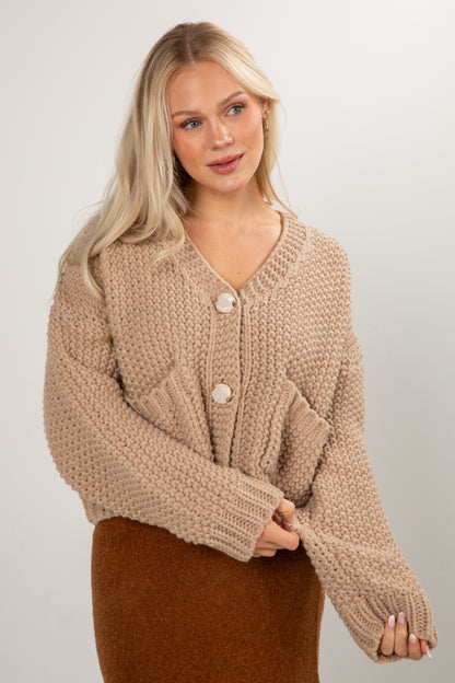 Woman wearing a beige knitted cardigan against a plain background