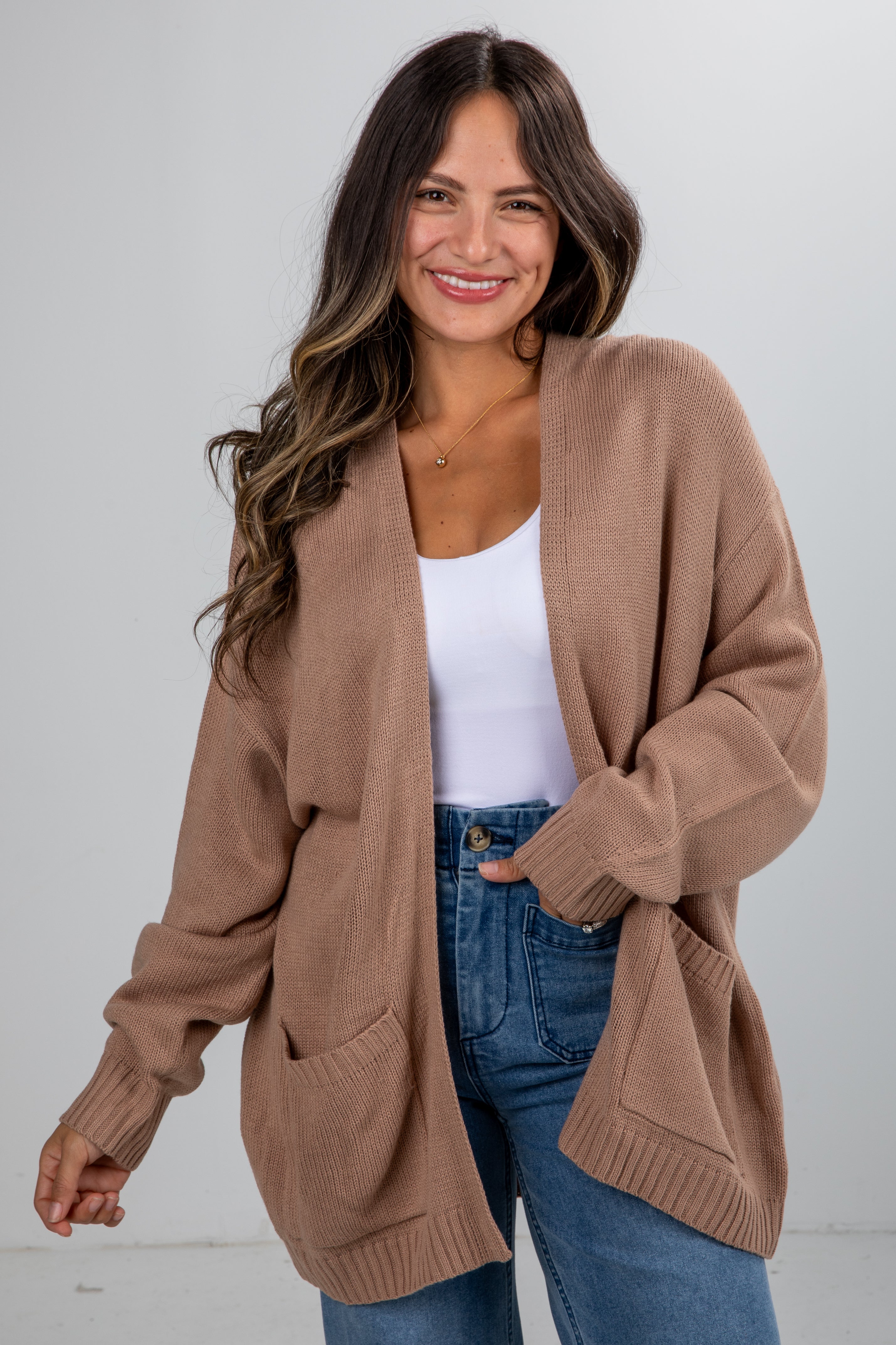 Woman wearing a brown cardigan over a white top and blue jeans on a white background