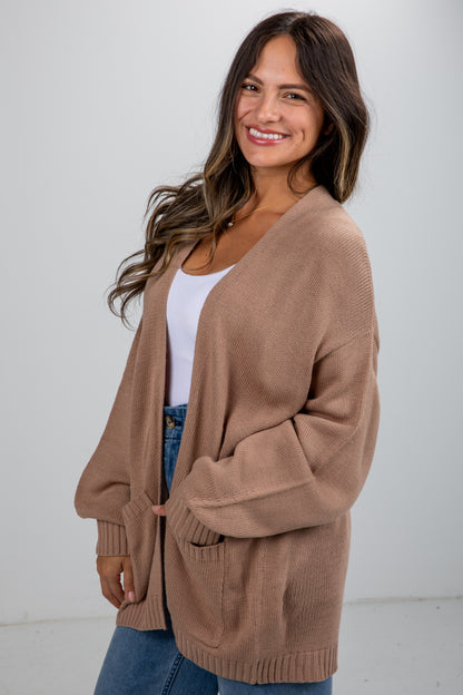 Woman wearing a brown cardigan over a white top and blue jeans on a white background