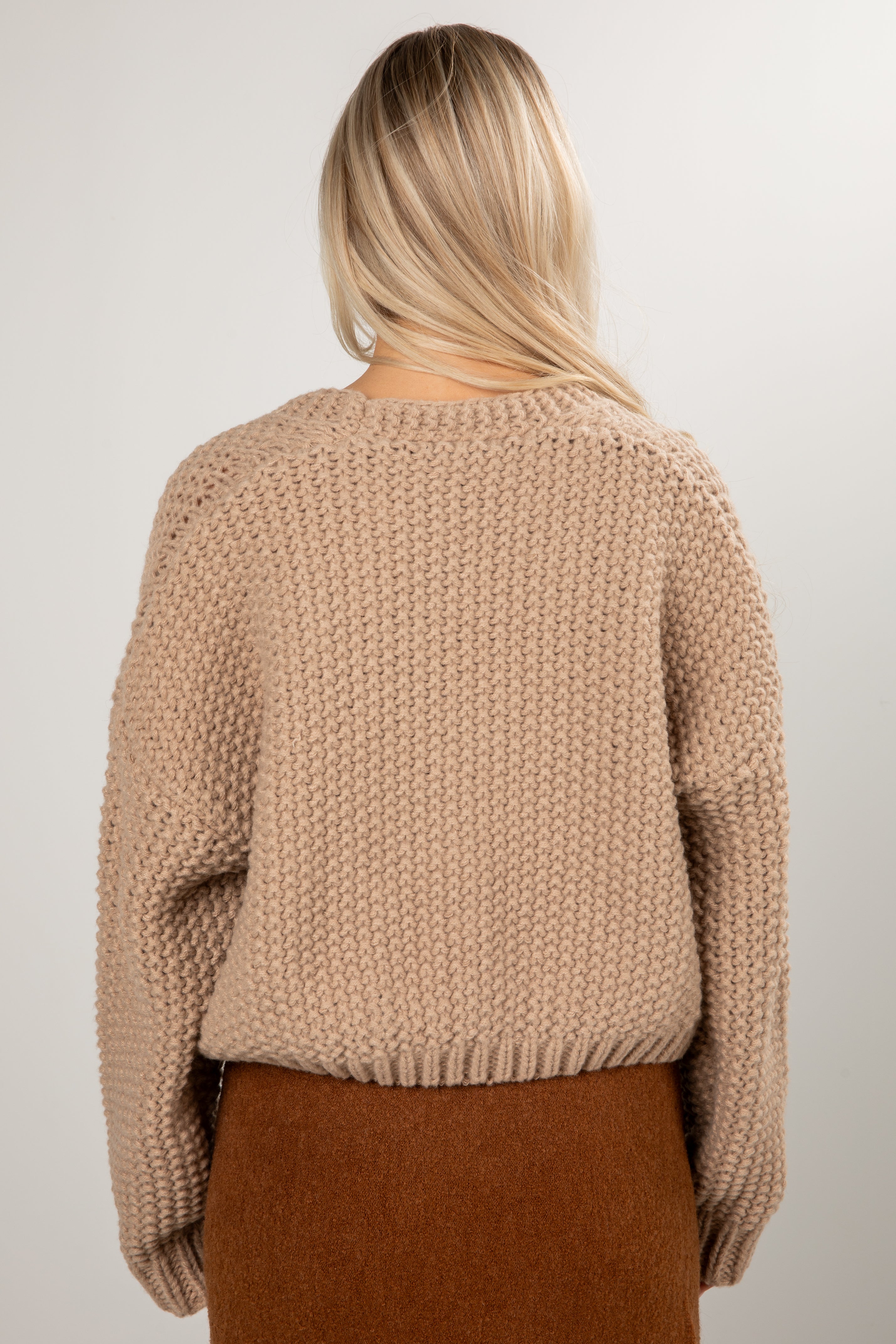 Person wearing a beige knitted sweater and brown skirt on a plain background