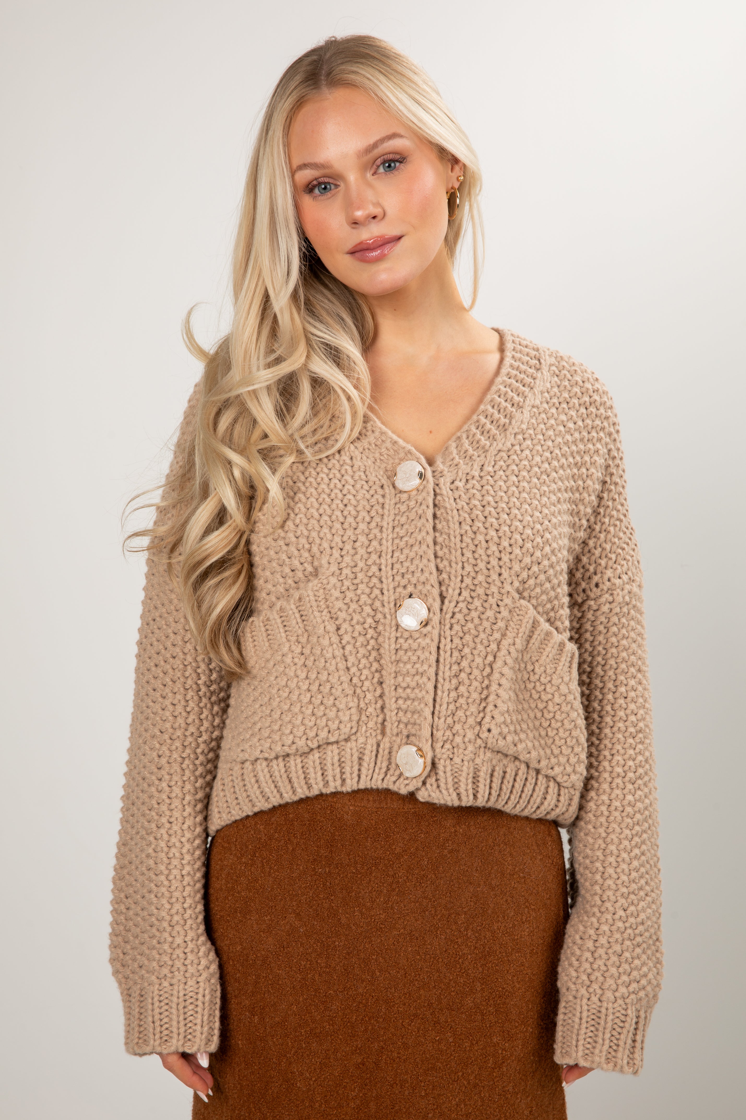 Woman wearing a beige knitted cardigan with a plain background
