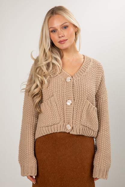 Woman wearing a beige knitted cardigan with a plain background
