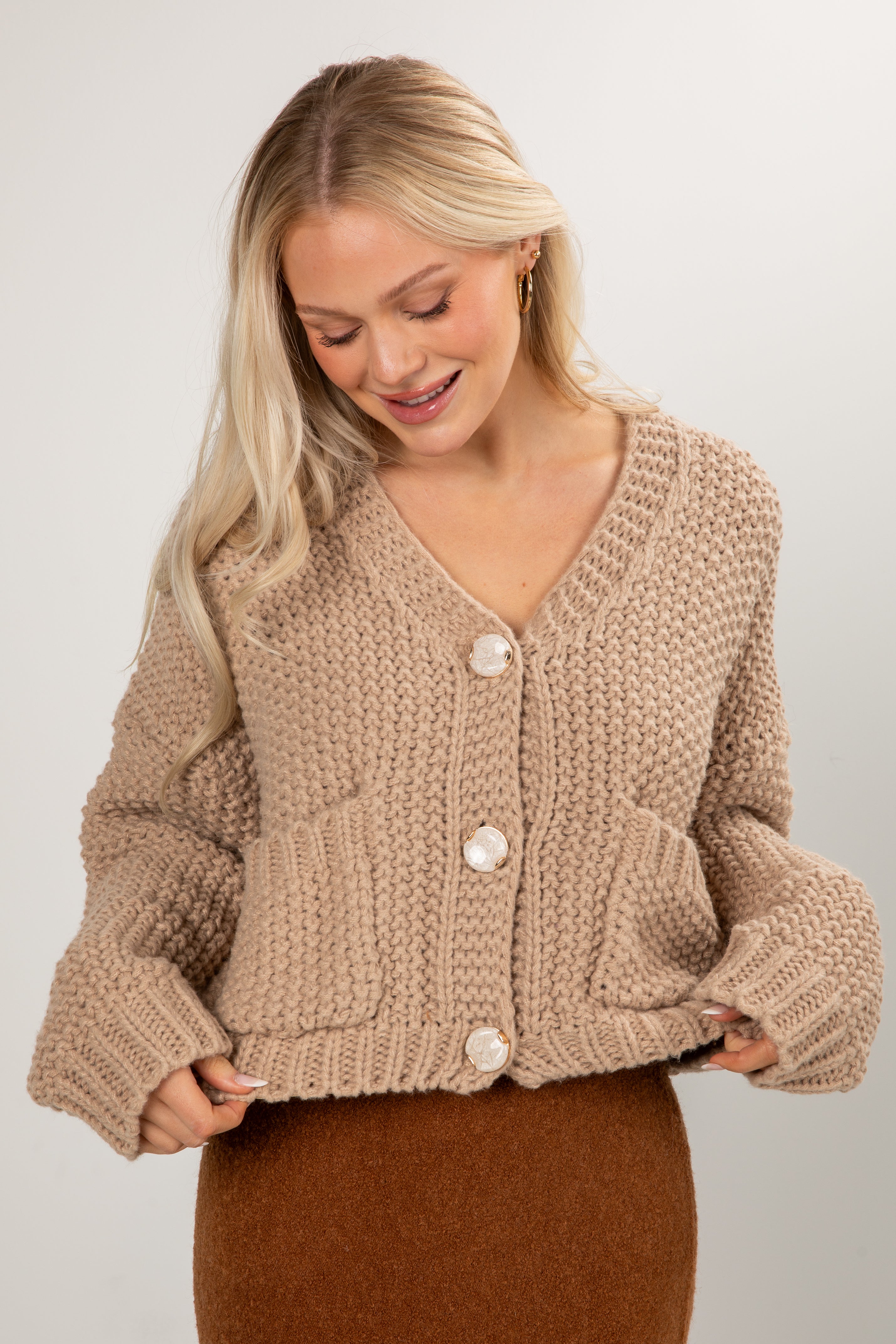 Woman wearing a beige knitted cardigan on a plain background