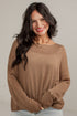 A woman with long dark hair smiling while wearing a loose-fitting, long-sleeve knit sweater in a warm taupe-brown color, paired with light-wash denim shorts.