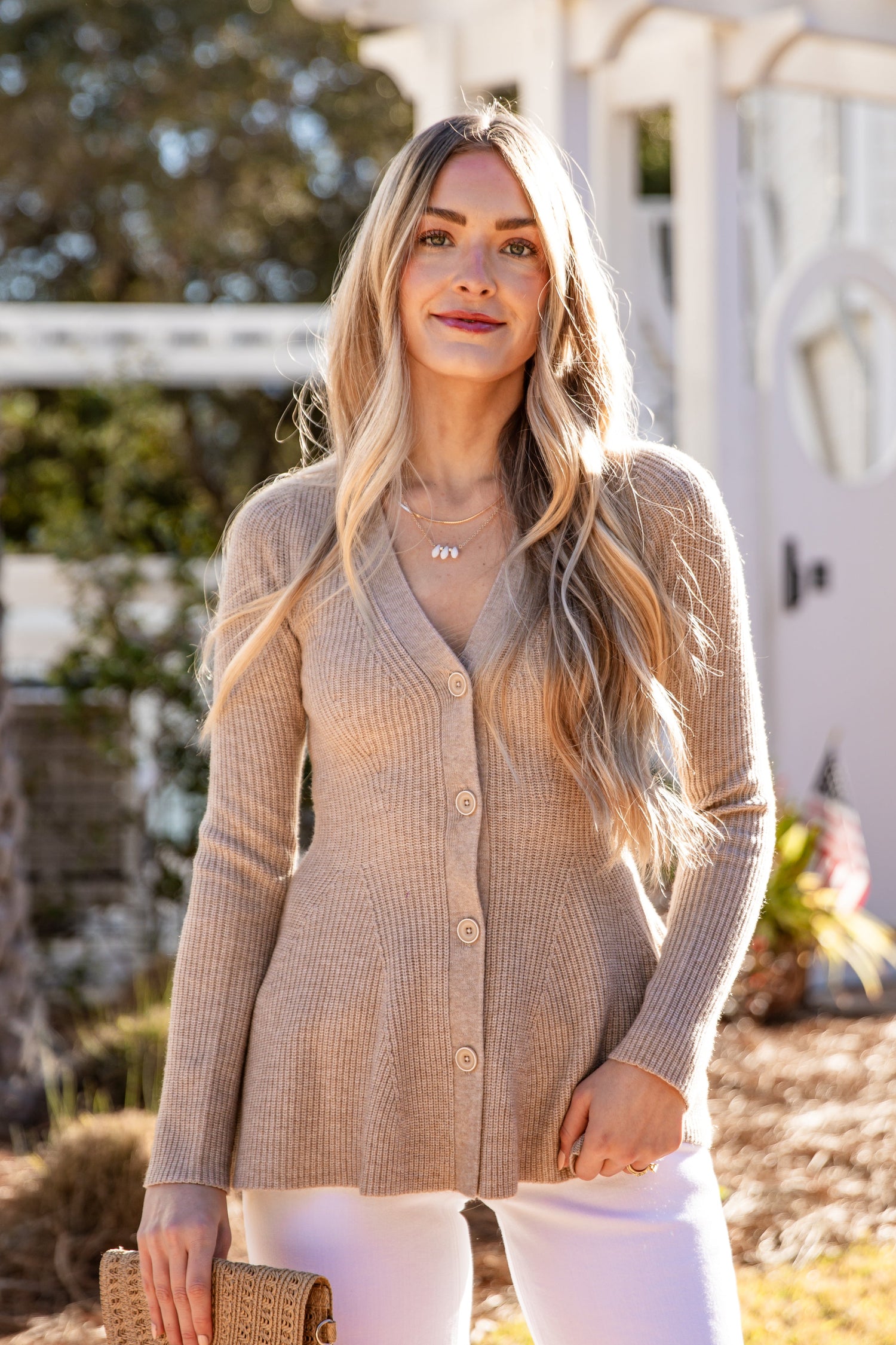 Woman wearing a beige cardigan and white pants standing outdoors.